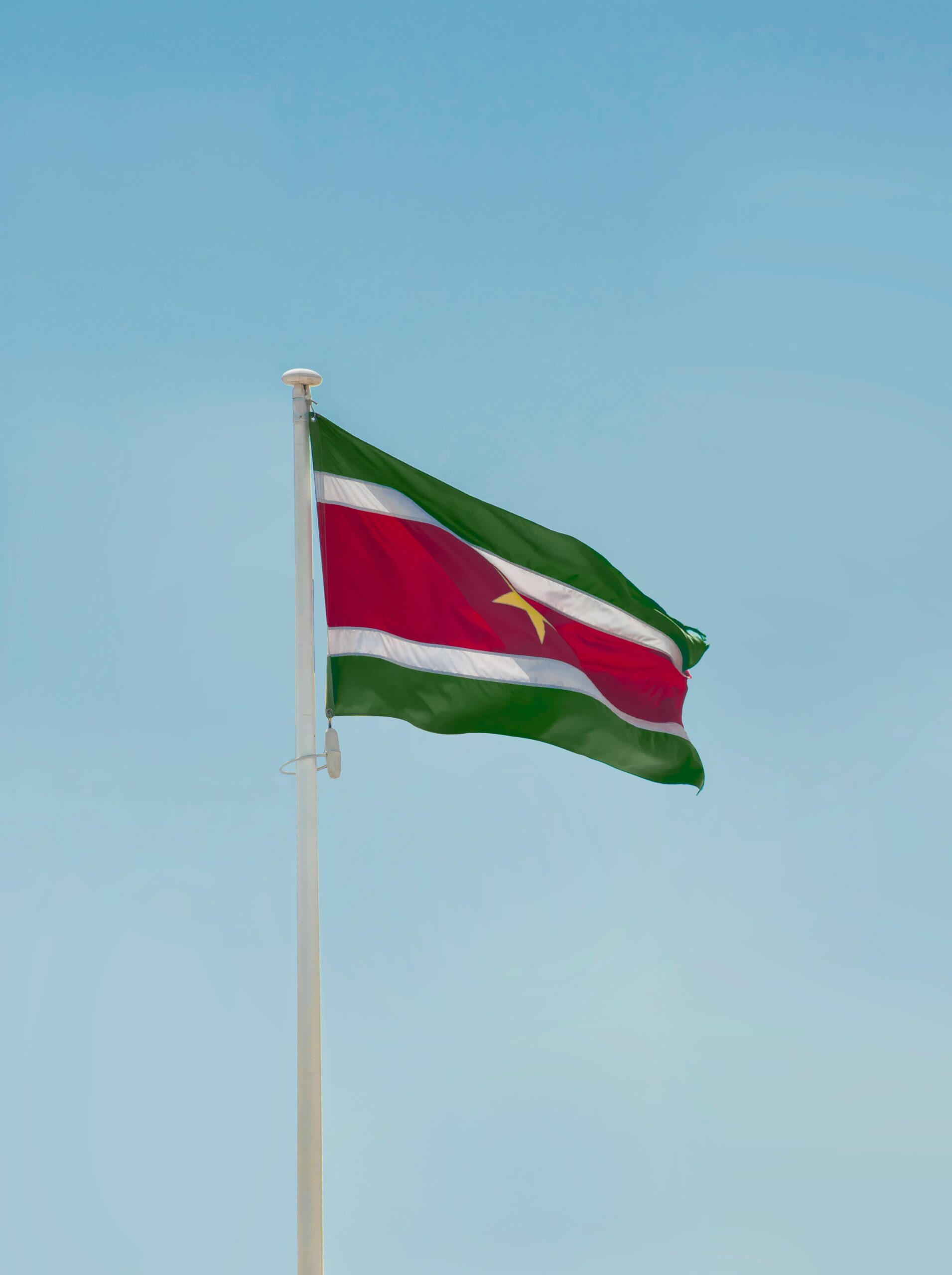 The Suriname national flag waving against a clear blue sky in Paramaribo.